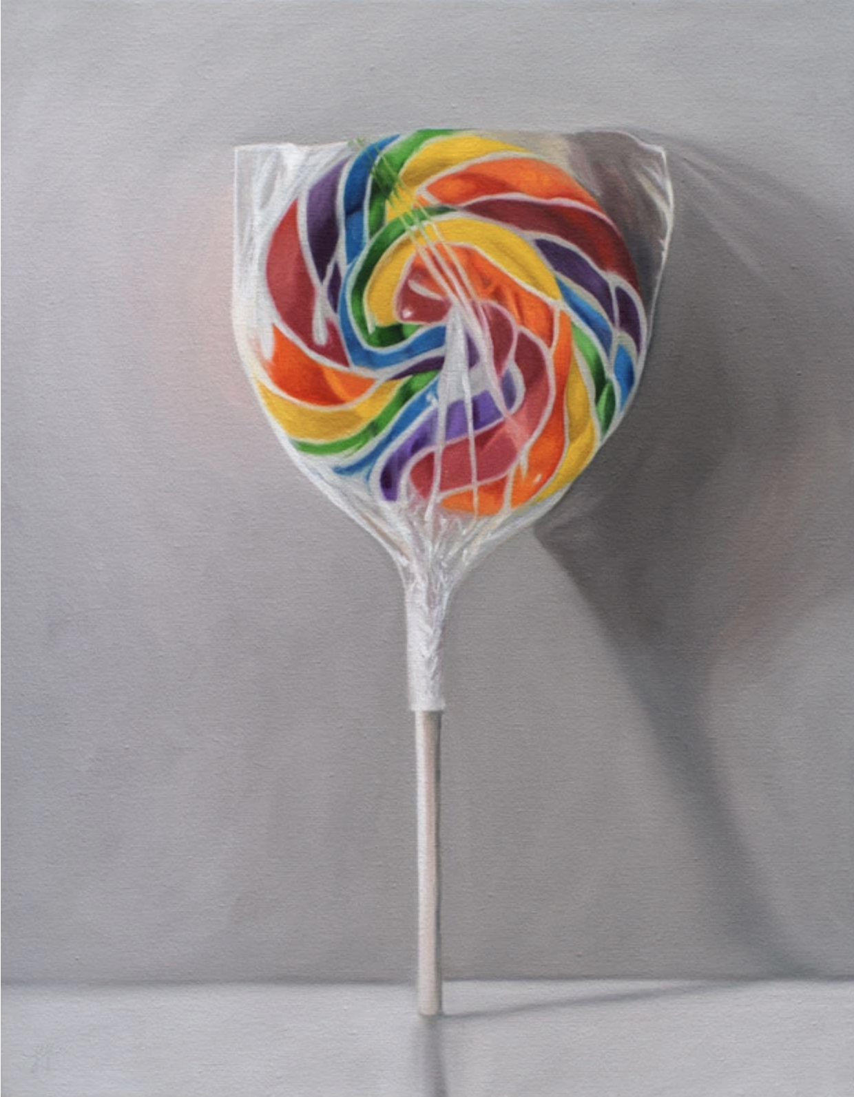 A single rainbow swirl lollipop rests agains a grey wall.
